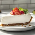 A slice of creamy no-bake cheesecake on a plate with a graham cracker crust and berry garnish.